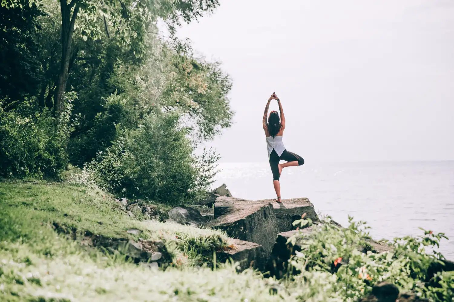 Silhouetted figure practicing yoga in tree pose on a rocky outcrop.